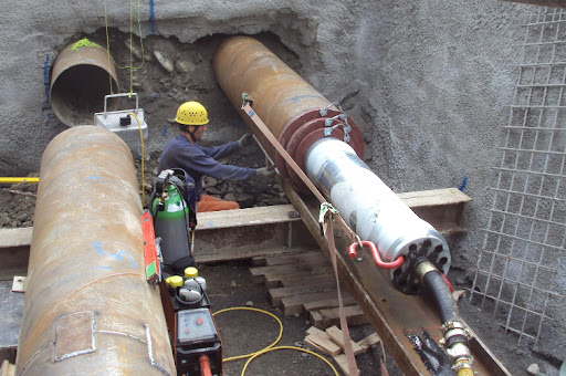 Ouvrier spécialisé supervisant le fonçage horizontal d'une conduite métallique dans un puits de travail bétonné